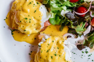 Delicious Eggs Benedict served on toasted bread with perfectly poached eggs, creamy hollandaise sauce, and a fresh side salad—part of the breakfast menu at Sicily Restaurant, available Friday to Sunday.