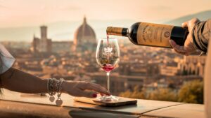 Red wine being poured into a glass at sunset with a scenic view of Florence, Italy in the background, featuring the iconic Duomo.