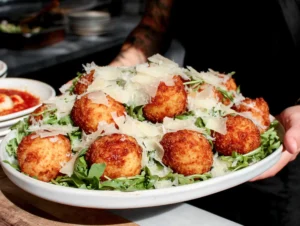 Chef holding large dish of arancini with rocket and shaved parmesan